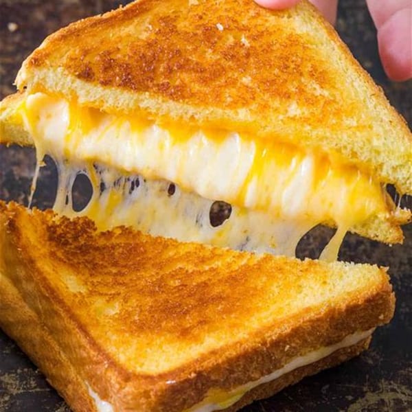 A grilled cheese sandwich from Carolina Cheese Co. pulled apart, showing gooey, melted cheese stretching.