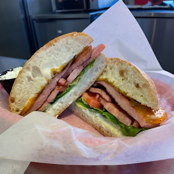 A Carolina Cheese Co. sandwich with meat, lettuce, and tomato on ciabatta bread.