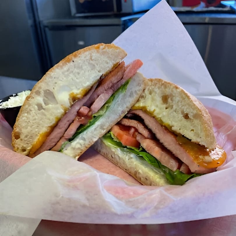 A Carolina Cheese Co. sandwich with meat, lettuce, and tomato on ciabatta bread.