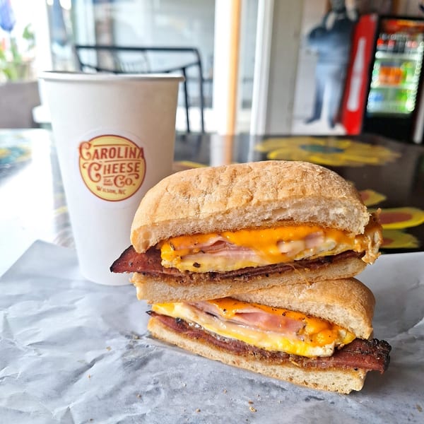 A Carolina Cheese Co. breakfast sandwich with egg, cheese, and meat, next to a branded cup.