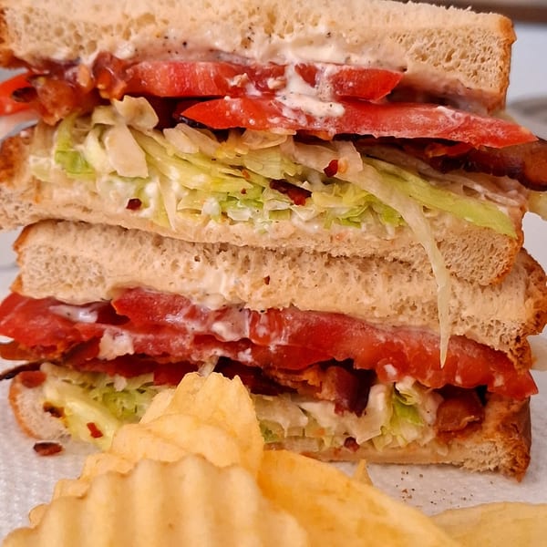 A Carolina Cheese Co. BLT sandwich with lettuce, tomato, bacon, and mayonnaise, served with chips.