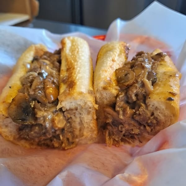 Two Carolina Cheese Co. cheesesteak sandwiches with mushrooms and onions in a paper-lined basket.