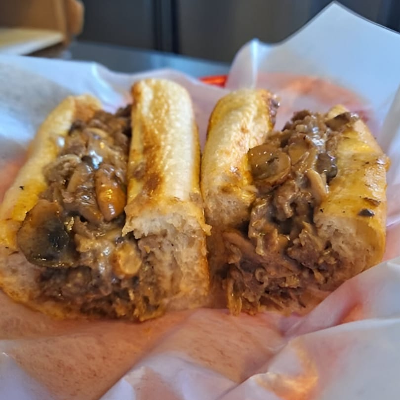 Two Carolina Cheese Co. cheesesteak sandwiches with mushrooms and onions in a paper-lined basket.
