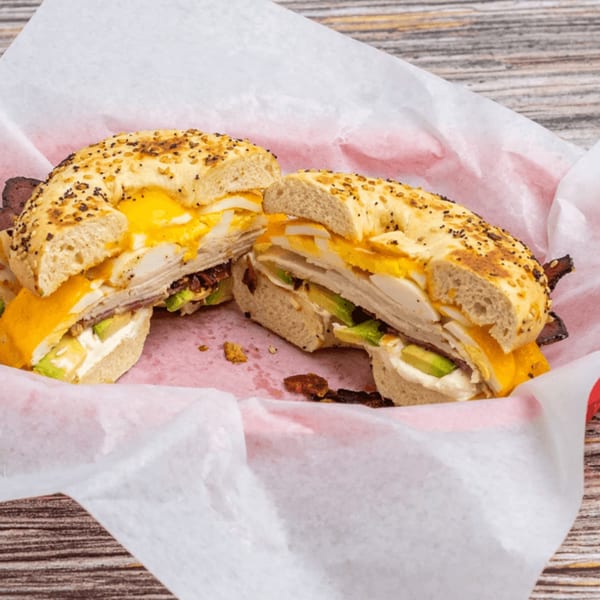 Everything bagel sandwich with egg, cheese, avocado, and bacon, served in a red basket.